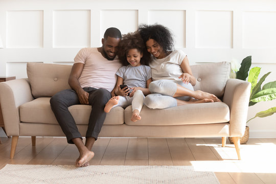 Happy Biracial Family With Daughter Using Cellphone At Home