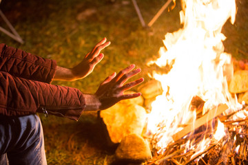 Tourist warming up his hands above camping fire