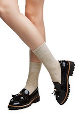 Cropped shot of a girl's cross-legs in black shoes, staying on a white background. It is beige socks on her foots. 