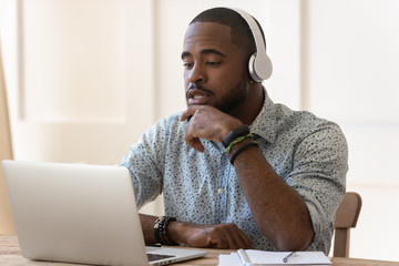 Concentrated biracial man in headphones watching webinar on laptop