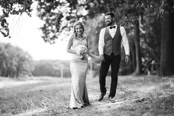 Sensual Black and white foto of bride and groom. Stylish couple of happy newlyweds posing and kisses in the park on their wedding day. Together. The concept of youth, love, fashion and lifestyle. 