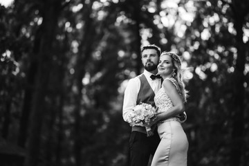 Sensual Black and white foto of bride and groom. Stylish couple of happy newlyweds posing and kisses in the park on their wedding day. Together. The concept of youth, love, fashion and lifestyle. 