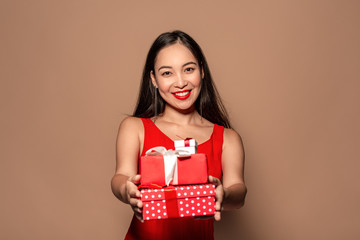 Freestyle. Young girl in dress standing isolated on brown giving present boxes to camera smiling friendly