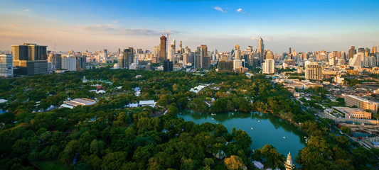 Fototapeta premium Zwiedzanie parku Lumpini wokół nowoczesnych biurowców i kondominium w centrum Bangkoku z chmurami o zachodzie słońca