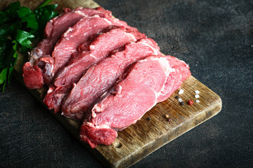 Fresh raw beef, cut into steaks  with vegetables, herbs and spices on a wooden board on a dark background. Copy space. Top view..