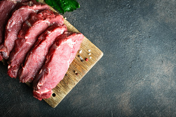 Fresh raw beef, cut into steaks  with vegetables, herbs and spices on a wooden board on a dark background. Copy space. Top view..