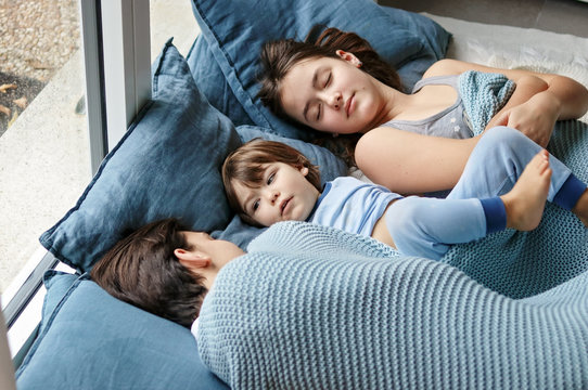 Three happy siblings snuggling under warm knitted blanket. Little boy and his tween sister and teenager brother enjoying staying at home at cold winter day relaxing together taking a nap. Family time