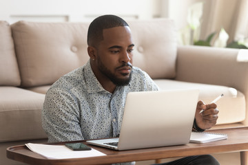 Focused biracial man studying at laptop making notes