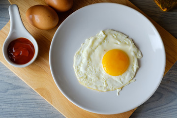 The fried egg is in a white round dish placed on a cutting board,top view food concept