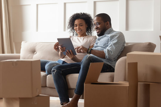 African couple sit on couch near boxes using tablet computer