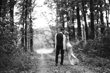 Sensual Black and white foto of bride and groom. Stylish couple of happy newlyweds posing in the park on their wedding day. Handsome bearded groom admires and kisses pretty bride. Together.