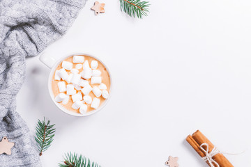 Winter composition with hot drink, marshmallows, green fir branches, wooden decorations and two cinnamon sticks on white background. Flat lay, copy space