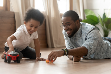 Father and son holding toy cars playing on warm floor