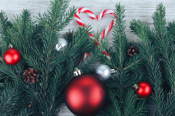 Closeup of Christmas baubles,  red ball, fir tree branches, hear shaped candy cane on white wooden table. Christmas background. New Year, winter holiday, top view