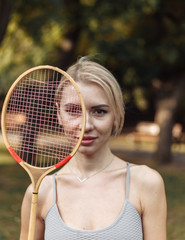 Portrait of attractive sport woman with badminton racket in the park on a bright sunny day