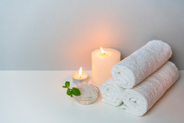 Fototapeta na wymiar SPA treatments concept photo on grey background with stack of white towels, candles and cup of sea salt.