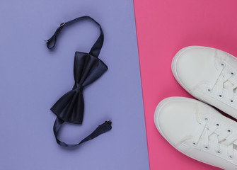 Minimalistic fashion still life, groom look. Stylish white sneakers and a bow tie on purple pink background. Top view