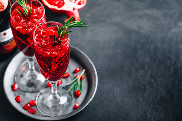 Pomegranate Champagne Cocktail with rosemary on gray concrete stone background