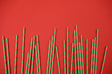 Red and green striped straws on red background, copy space. Christmas texture. Minimalism concept. Top view, flat lay