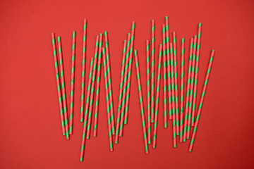 Red and green striped straws on red background, copy space. Christmas texture. Minimalism concept. Top view, flat lay