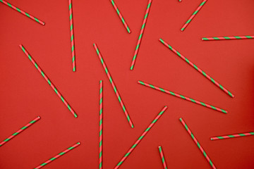 Red and green striped straws on red background, copy space. Christmas texture. Minimalism concept. Top view, flat lay