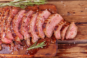 Chopped Grilled Steak Rib Eye on Rustic Wooden Cutting Board on Wooden Background. Medium Ribeye Steak with Spices and Rosemary. Concept of Delicious Meat Food