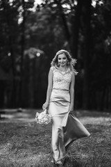 Obraz na płótnie Canvas Black and white foto of beautiful bride with a wedding bouquet for a walk in the park. Happy newlywed woman stands among green bushes in the garden. Smiling bride. Wedding day. Fashion bride.