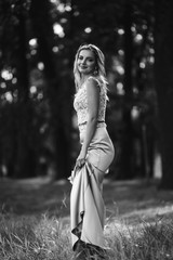 Black and white foto of beautiful bride with a wedding bouquet for a walk in the park. Happy newlywed woman stands among green bushes in the garden. Smiling bride. Wedding day. Fashion bride.