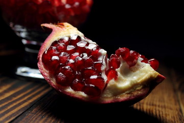 Slice of pomegranate fruit with red grains on a wooden table
