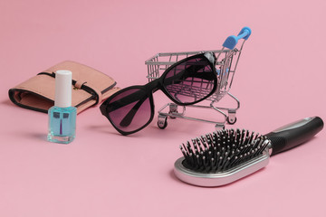 Minimalistic shopping concept. Mini shopping trolley with female accessories on pink pastel background