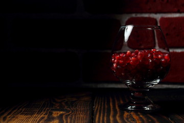 Glass with red pomegranate grains on a wooden table. Fruit wine, alcohol