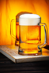 Two Light Beer Mugs with White Foam on Dark Wooden Table and Yellow Background