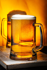 Two Light Beer Mugs with White Foam on Dark Wooden Table and Yellow Background