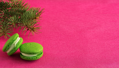 Green macaron with fondant on red paper background, next to a Christmas tree branch. Close-up, copy space for text. Postcard or banner concept.