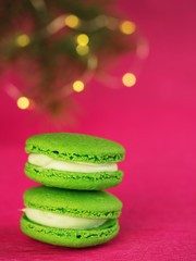 Green macaron with fondant on red paper background. Near a branch of a Christmas tree with a garland. Close-up, concept for postcard or banner.