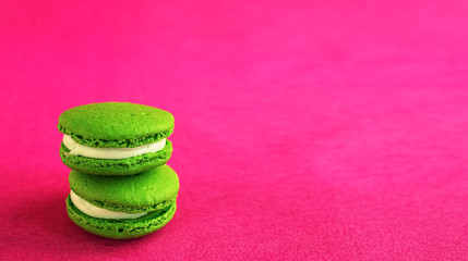 Two green macaron with fondant on a red paper background. Close-up, copy space for text. Postcard or banner concept.