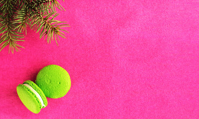 Two green macaron with fondant on a red paper background. Near the branch of the Christmas tree. Flat lay, copy space for text. Postcard or banner concept.