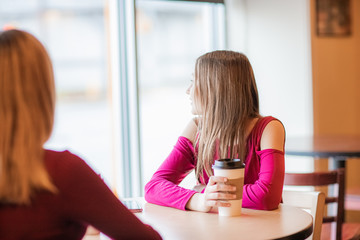 Cute, sad,  serious beautiful teenager girls, sitting in cafe drinking coffee and looking on window