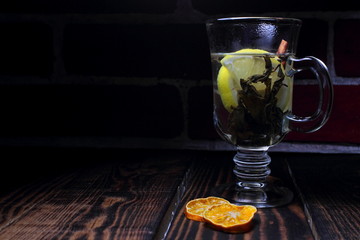 A glass with green tea leaves and a slice of lemon stands on a wooden table