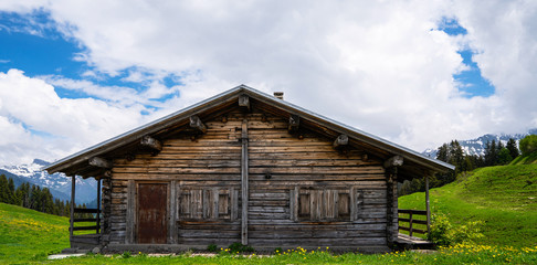 Fabulous alpine wooden house, green hills Switzerland, Europe. Panoramic view of idyllic mountain scenery in the Alps with fresh green meadows in bloom on a beautiful sunny day in springtime.