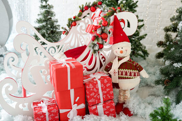 Fototapeta na wymiar christmas decor sleigh, snowman and gift boxes near green christmas tree on the snow
