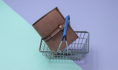 Minimalistic shopping concept. Mini shopping basket and leather wallet on purple blue background.