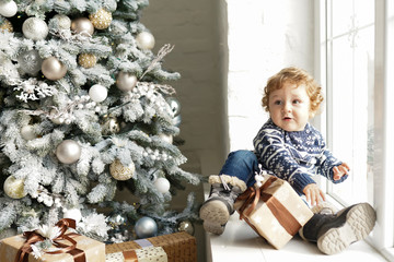 Christmas Baby , Child holding Gift Box sitting near christmas tree on the sofa at home