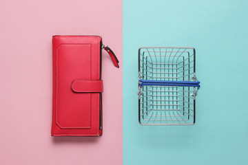 Minimalistic shopping concept. Mini shopping basket and red leather wallet on pink blue background. Top view