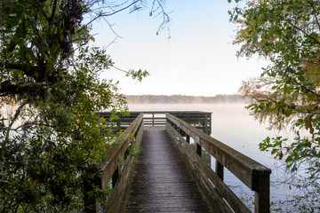 Fototapeta premium Misty Morning Lake with Autumn Colored Trees, Foliage, and Dock