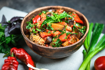 Vegetable saute or caponata, or pisto with eggplant, peppers, tomatoes and herbs in rustic bowl on a dark background.