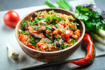 Vegetable saute or caponata, or pisto with eggplant, peppers, tomatoes and herbs in rustic bowl on a dark background.