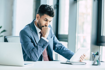Naklejka premium thoughtful businessman looking at digital tablet while sitting at workplace