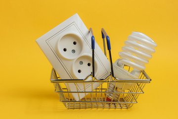Shopping trolley with double electrical outlet, spiral light bulb on yellow background