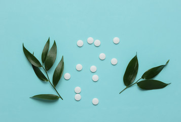 Herbal pills. White pills with green leaves on a blue pastel background. Minimalistic medicine still life